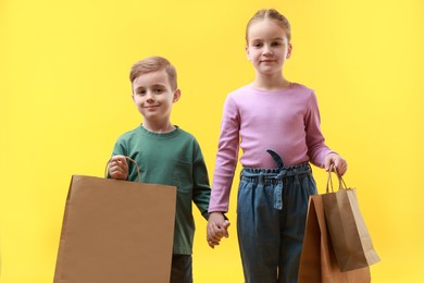 Photo of Cute little friends with shopping bags holding hands on yellow background