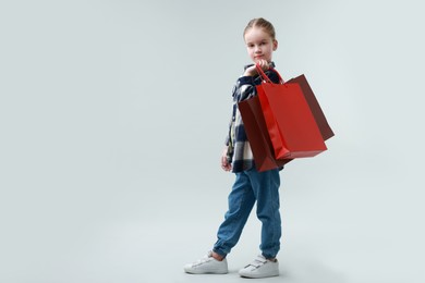 Photo of Cute little girl with shopping bags on grey background. Space for text