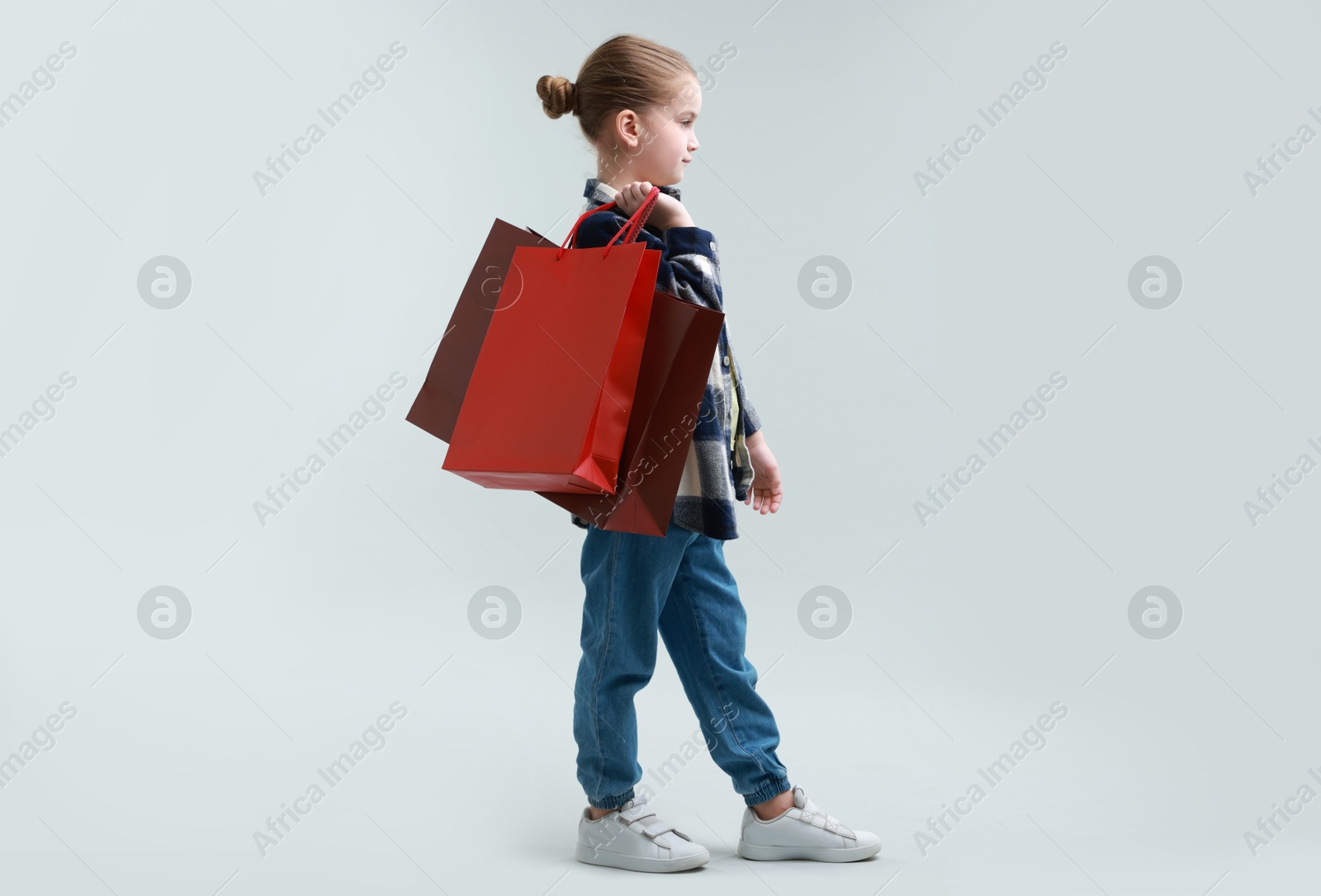 Photo of Cute little girl with shopping bags on grey background