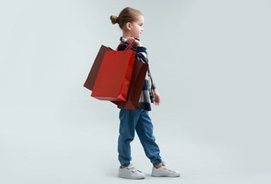 Photo of Cute little girl with shopping bags on grey background