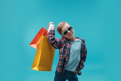 Photo of Cute little boy with shopping bags on light blue background