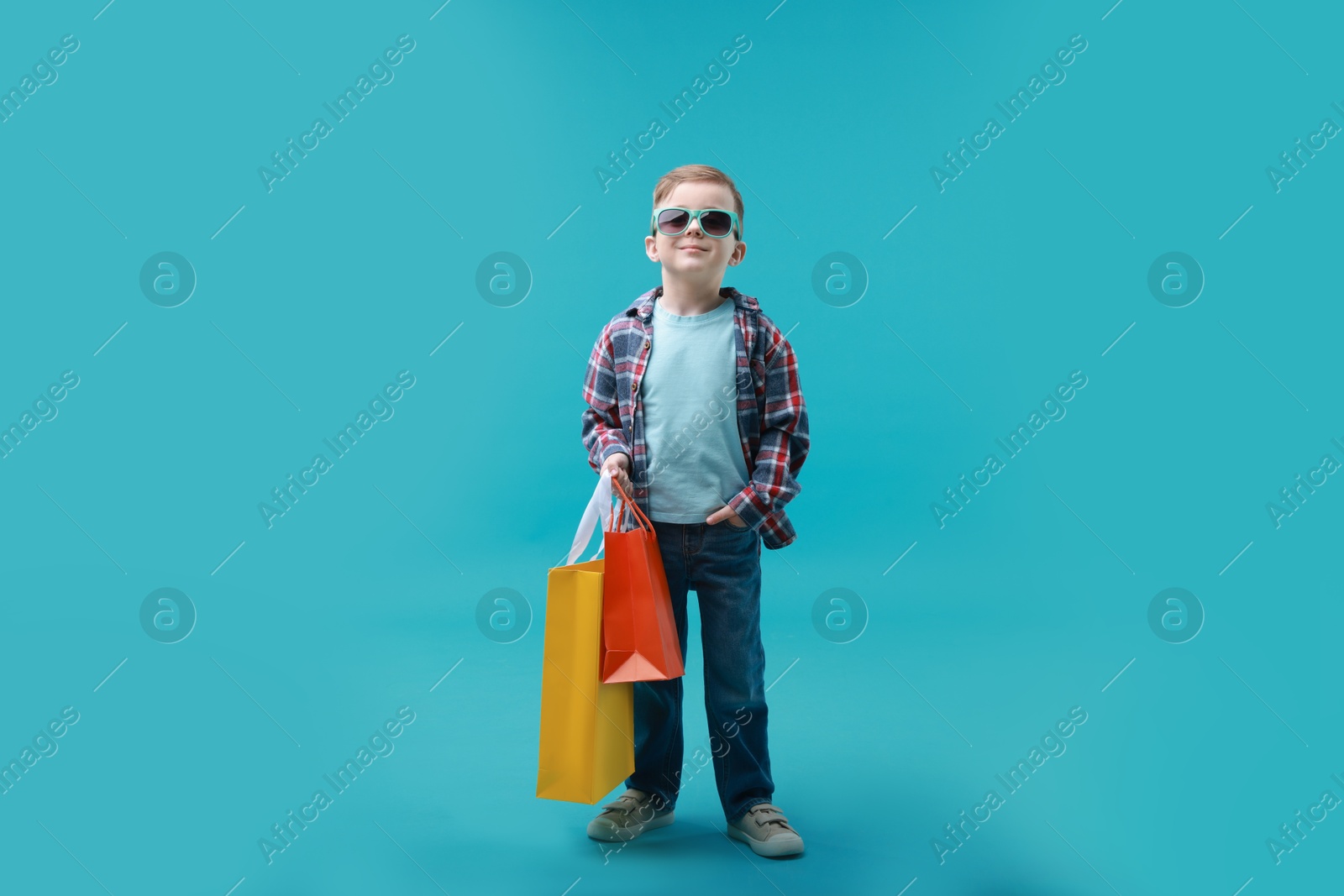 Photo of Cute little boy with shopping bags on light blue background. Space for text