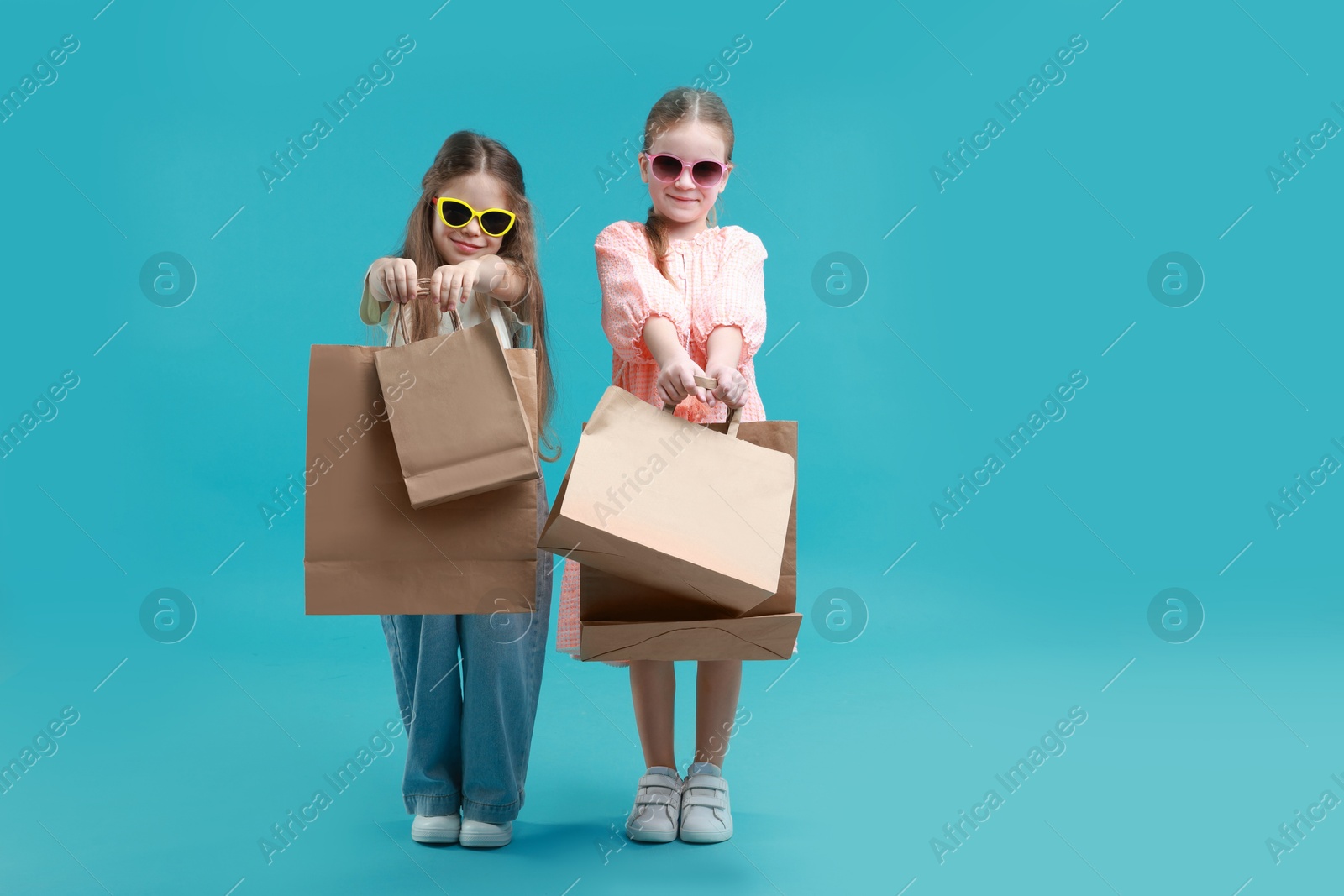 Photo of Cute little friends with shopping bags on light blue background. Space for text