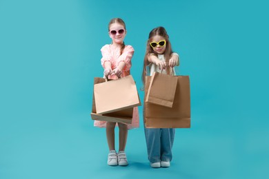 Photo of Cute little friends with shopping bags on light blue background. Space for text