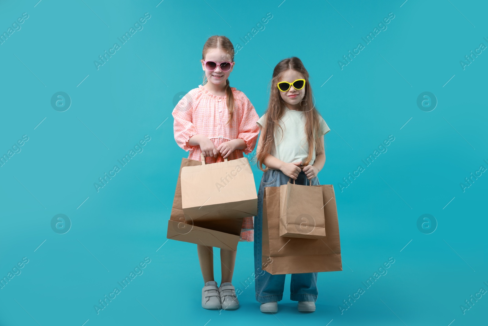 Photo of Cute little friends with shopping bags on light blue background