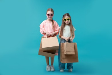 Photo of Cute little friends with shopping bags on light blue background