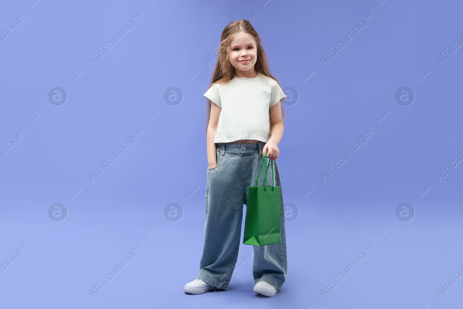 Photo of Cute little girl with shopping bag on violet background