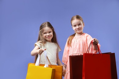 Photo of Cute little friends with shopping bags on violet background