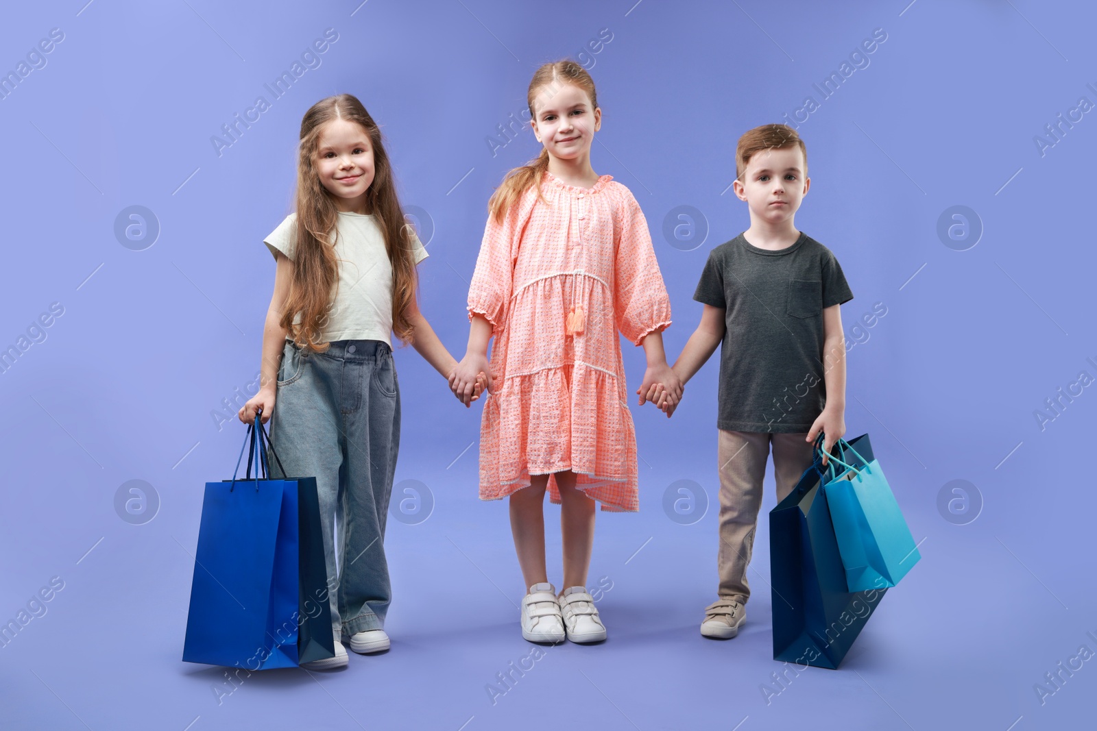 Photo of Cute little friends with shopping bags on violet background