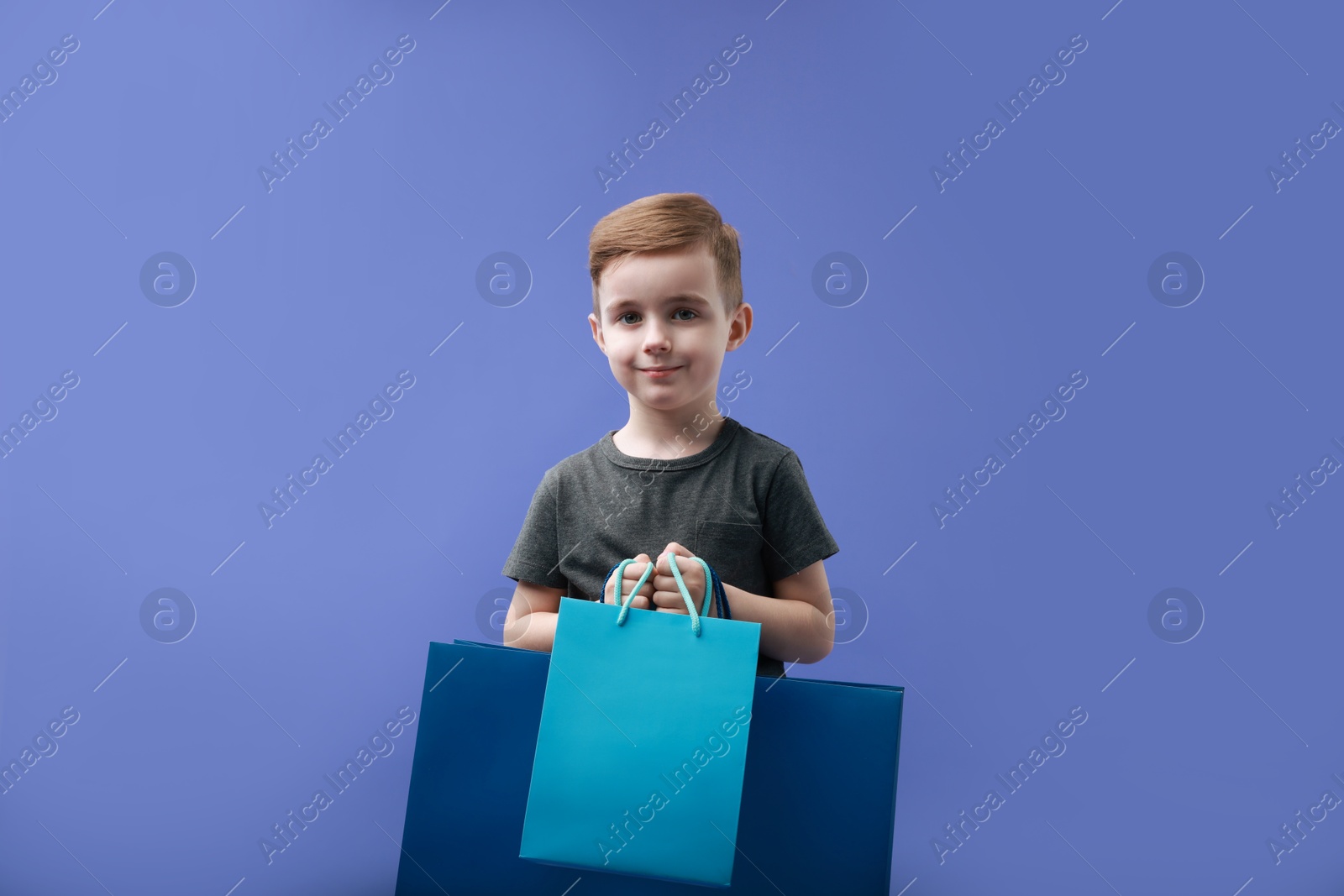 Photo of Cute little boy with shopping bags on violet background