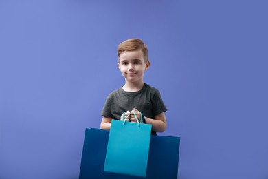 Photo of Cute little boy with shopping bags on violet background