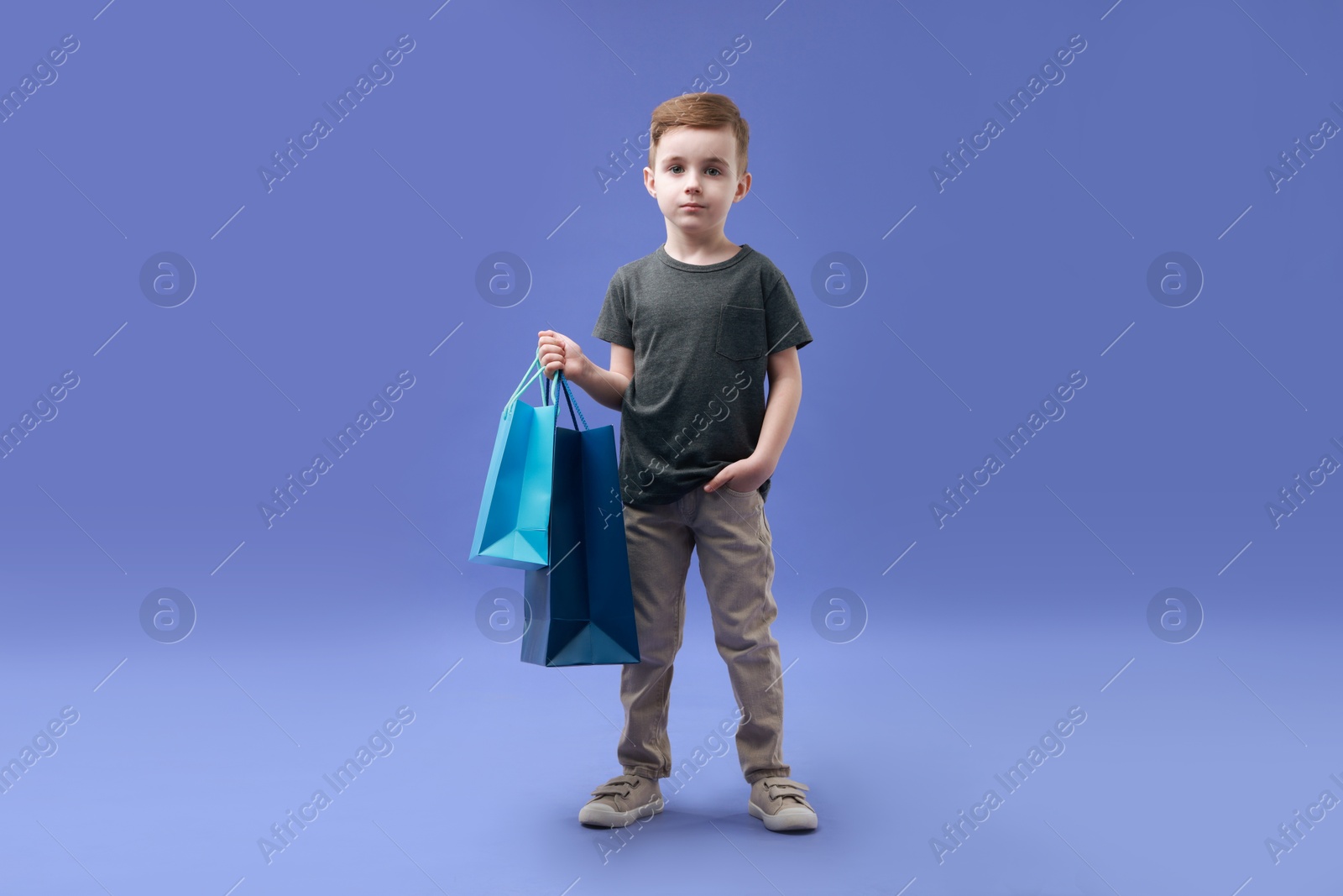 Photo of Cute little boy with shopping bags on violet background