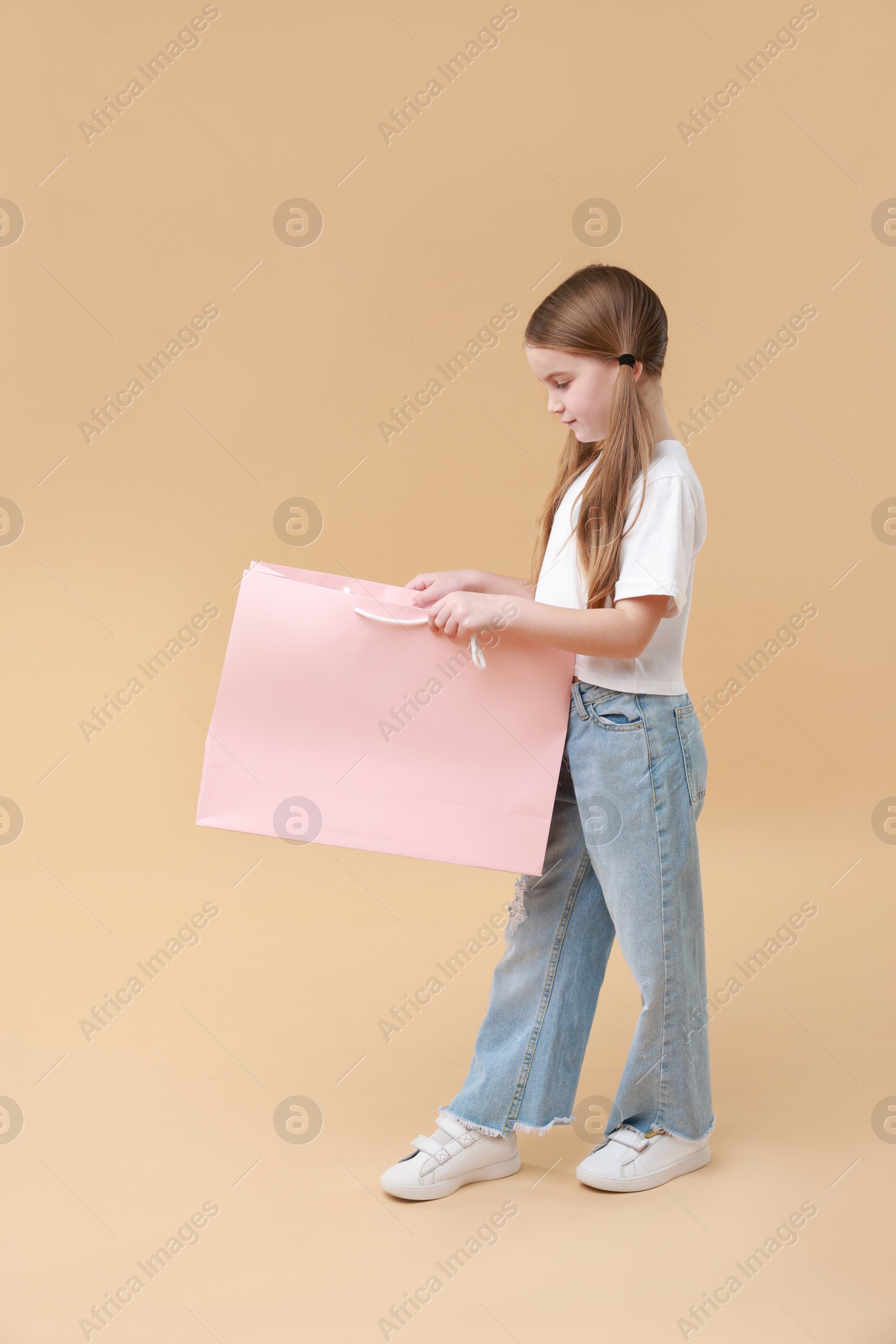 Photo of Cute little girl with shopping bag on beige background