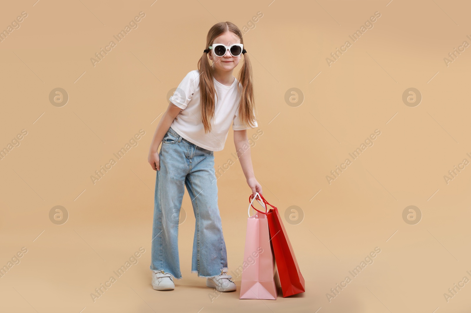 Photo of Cute little girl with shopping bags on beige background