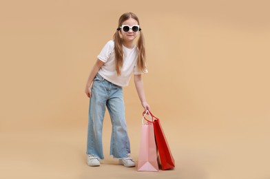 Photo of Cute little girl with shopping bags on beige background