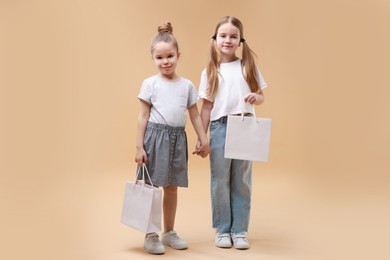 Photo of Cute little friends with shopping bags on beige background. Space for text