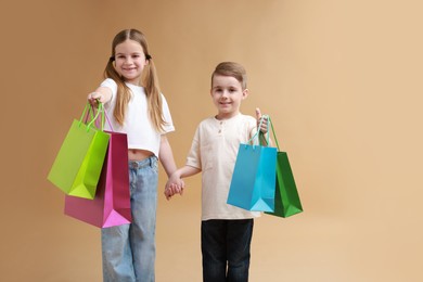 Photo of Cute little friends with shopping bags holding hands on beige background