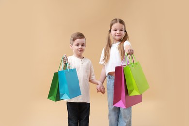 Photo of Cute little friends with shopping bags holding hands on beige background