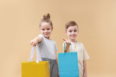 Photo of Happy little friends with shopping bags on beige background