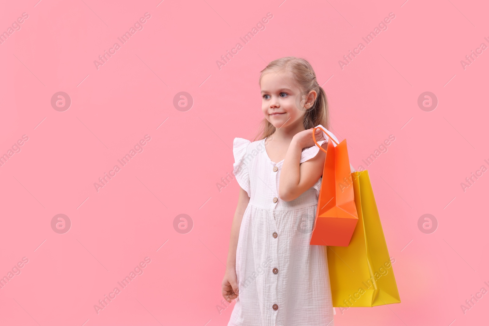 Photo of Little girl with shopping bags on pink background, space for text