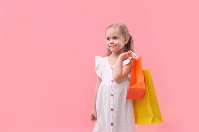 Photo of Little girl with shopping bags on pink background, space for text