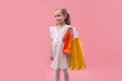 Photo of Little girl with shopping bags on pink background