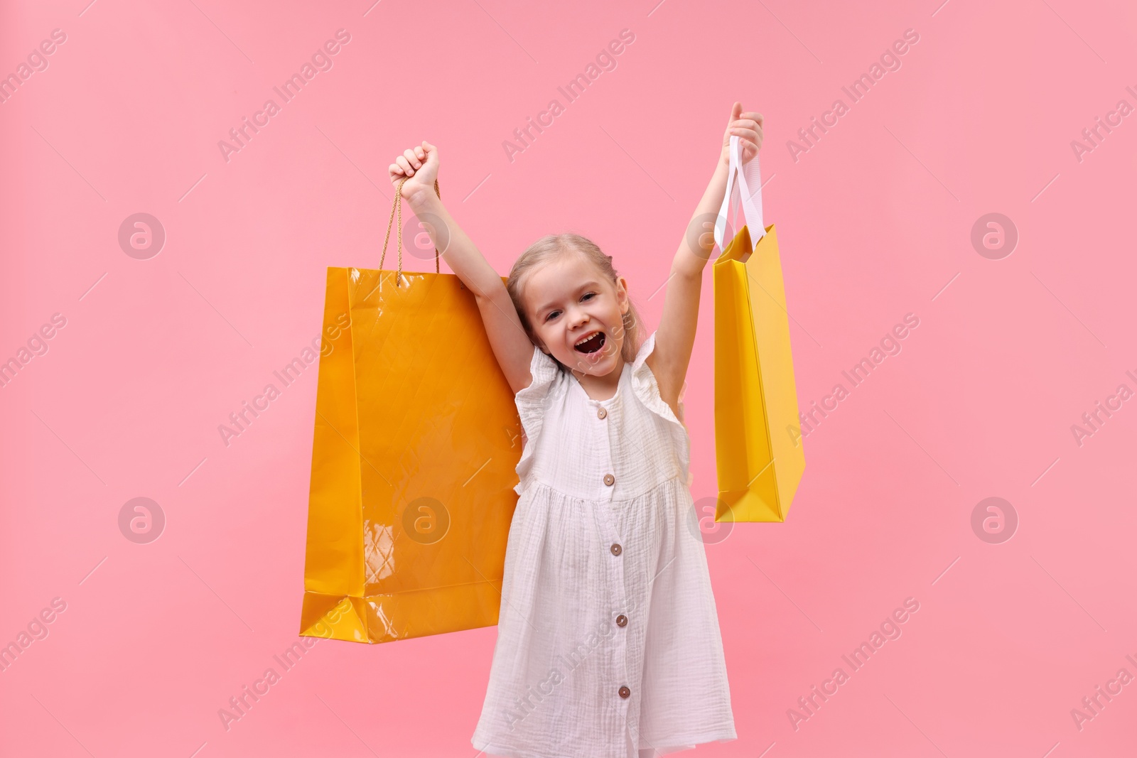 Photo of Little girl with shopping bags on pink background