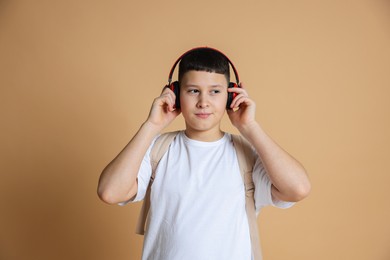 Photo of Portrait of teenage boy with headphones and backpack on beige background