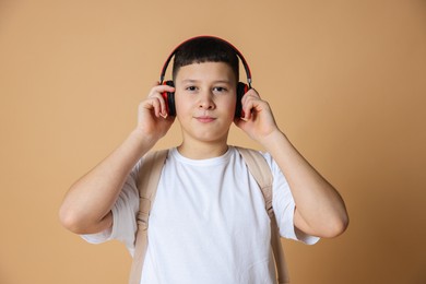 Photo of Portrait of teenage boy with headphones and backpack on beige background