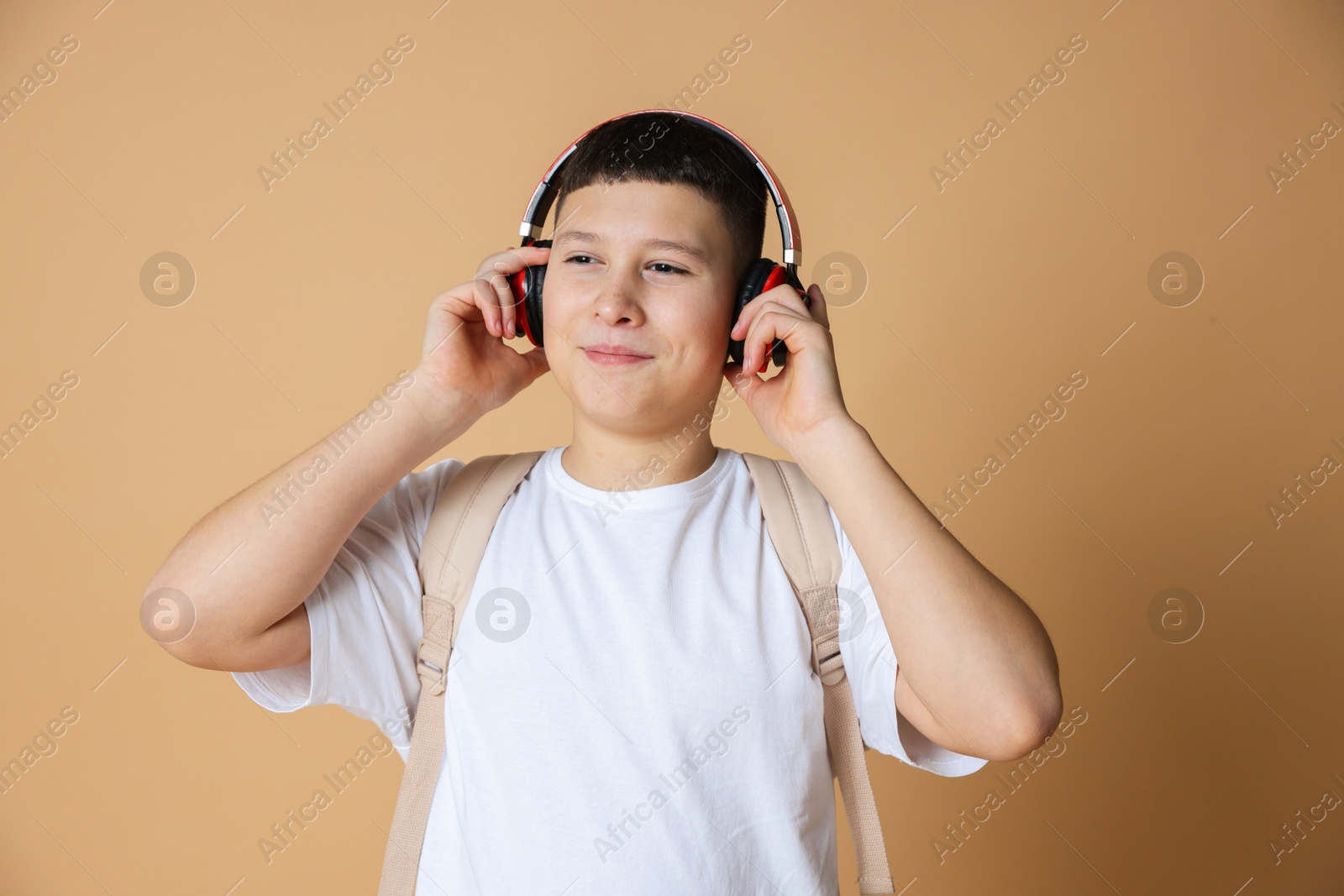 Photo of Portrait of teenage boy with headphones and backpack on beige background