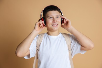 Photo of Portrait of teenage boy with headphones and backpack on beige background