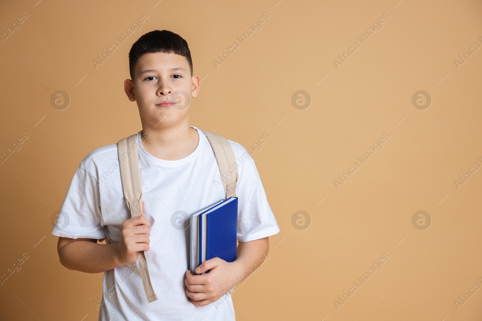 Photo of Portrait of teenage boy with books and backpack on beige background, space for text