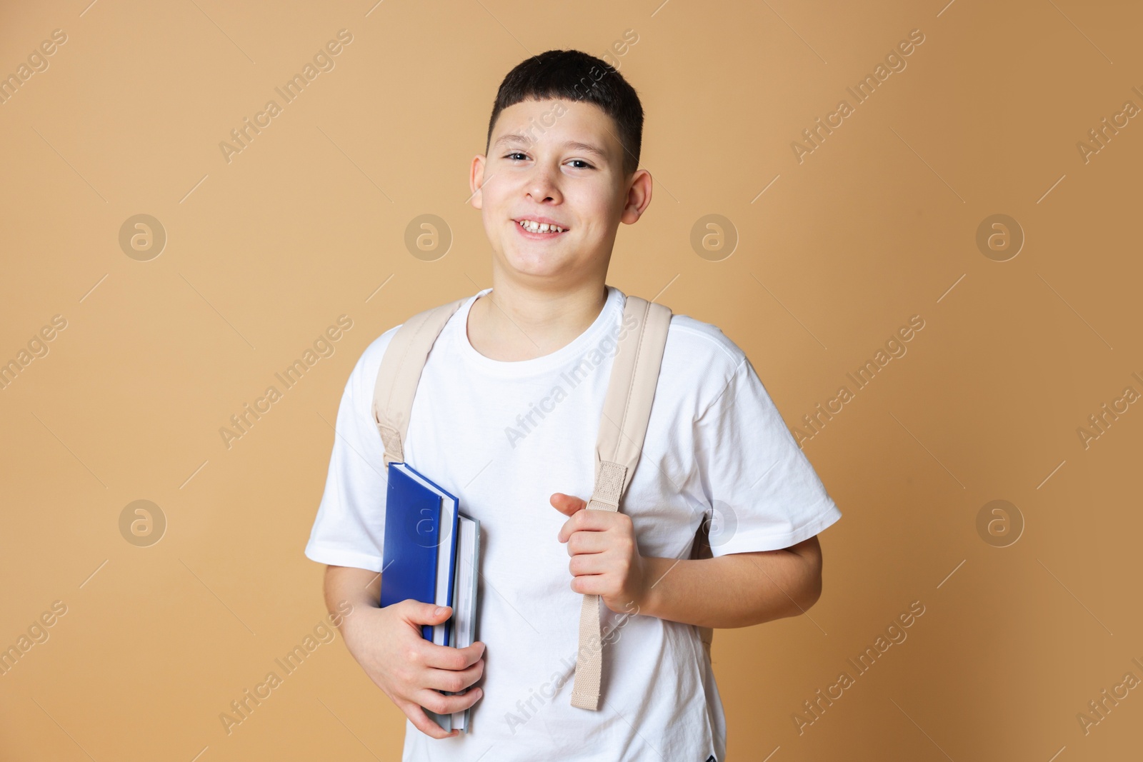 Photo of Portrait of teenage boy with books and backpack on beige background