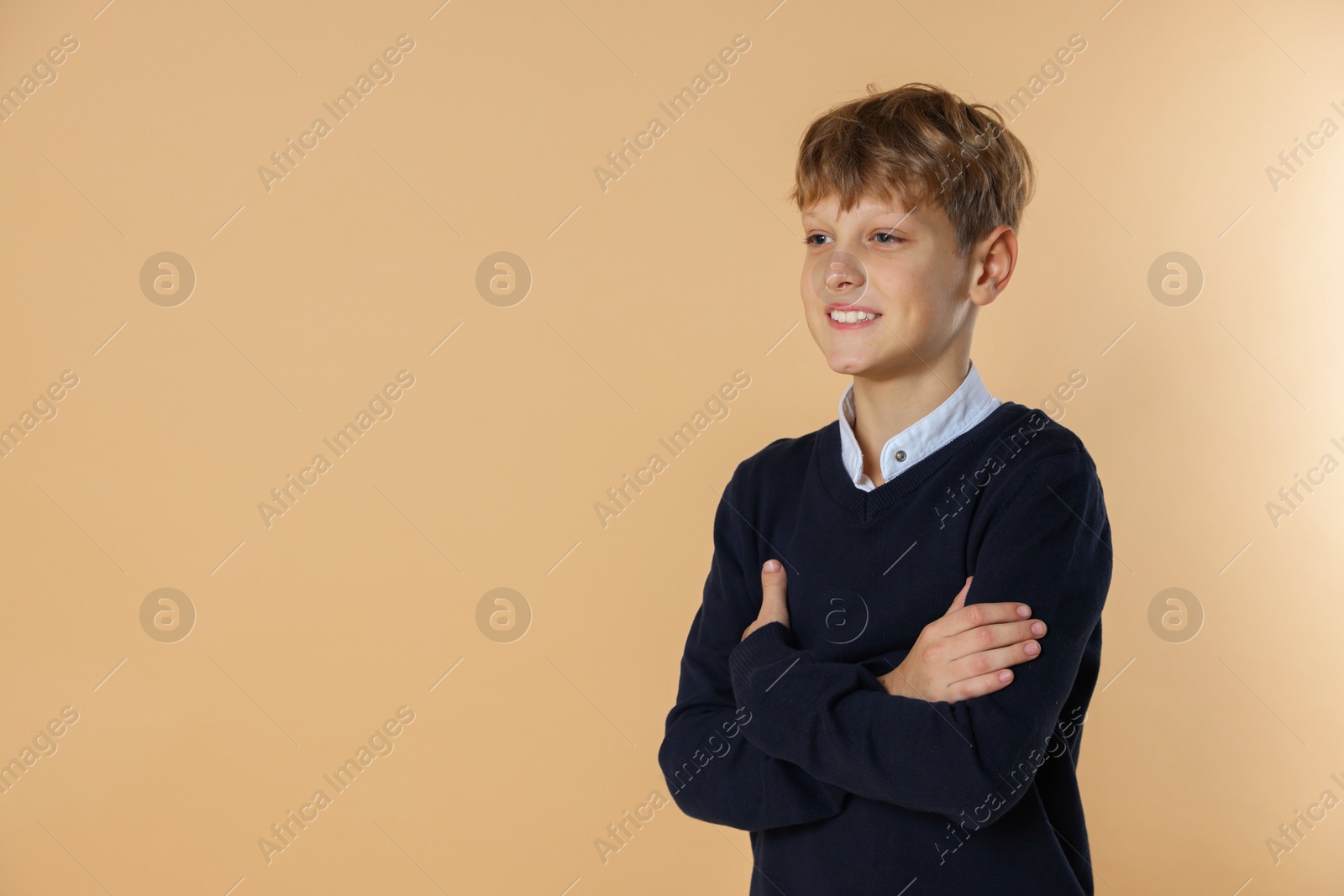 Photo of Portrait of teenage boy with crossed arms on beige background, space for text