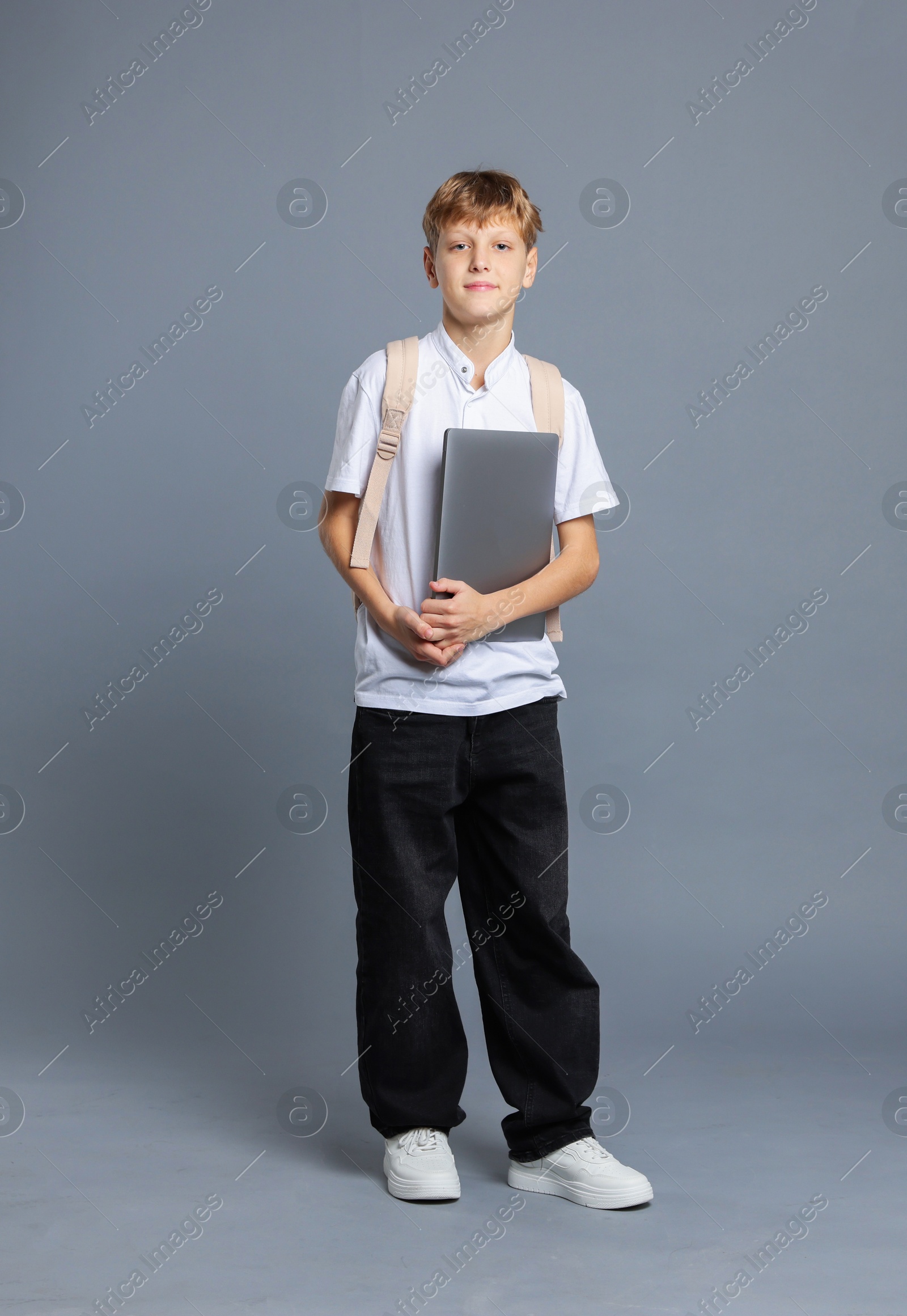 Photo of Full length portrait of teenage boy with laptop and backpack on grey background