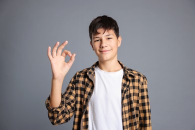 Photo of Portrait of teenage boy showing ok gesture on grey background