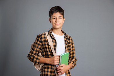 Photo of Portrait of teenage boy with book and backpack on grey background