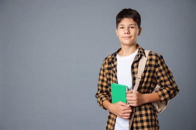 Photo of Portrait of teenage boy with book and backpack on grey background, space for text