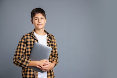 Photo of Portrait of teenage boy with laptop on grey background, space for text