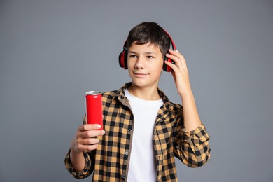 Photo of Portrait of teenage boy with can of drink and headphones on grey background