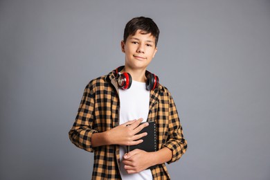 Photo of Portrait of teenage boy with notebook and headphones on grey background