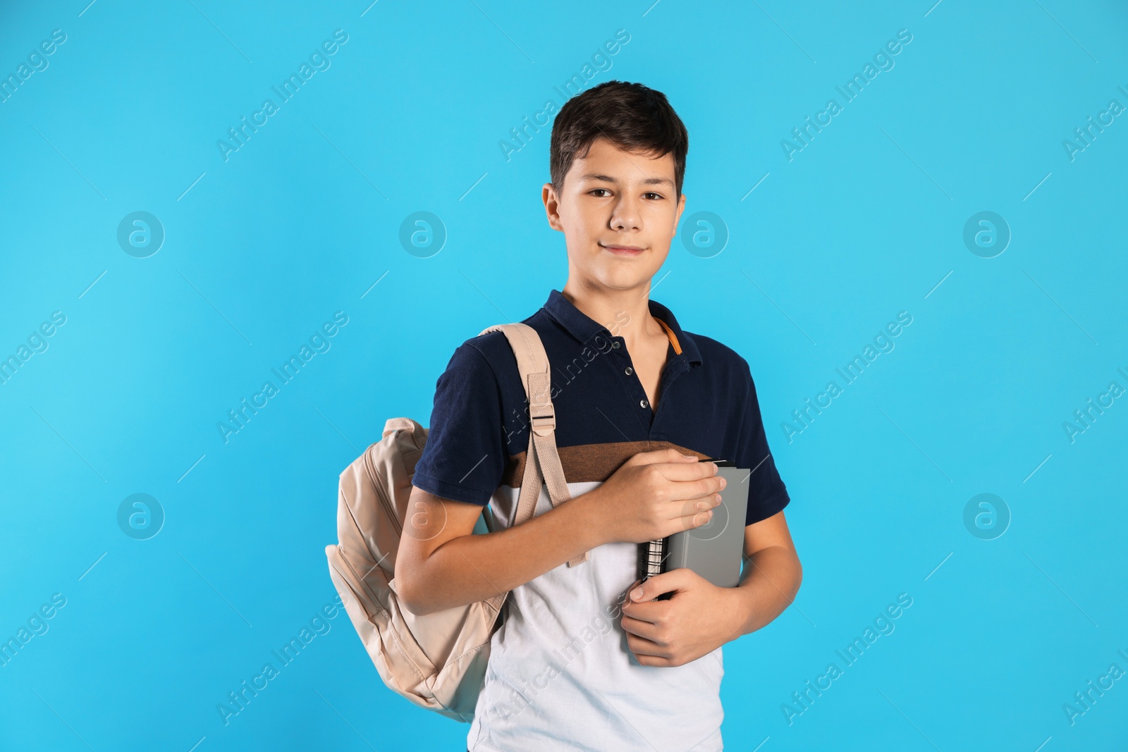 Photo of Portrait of teenage boy with books and backpack on light blue background