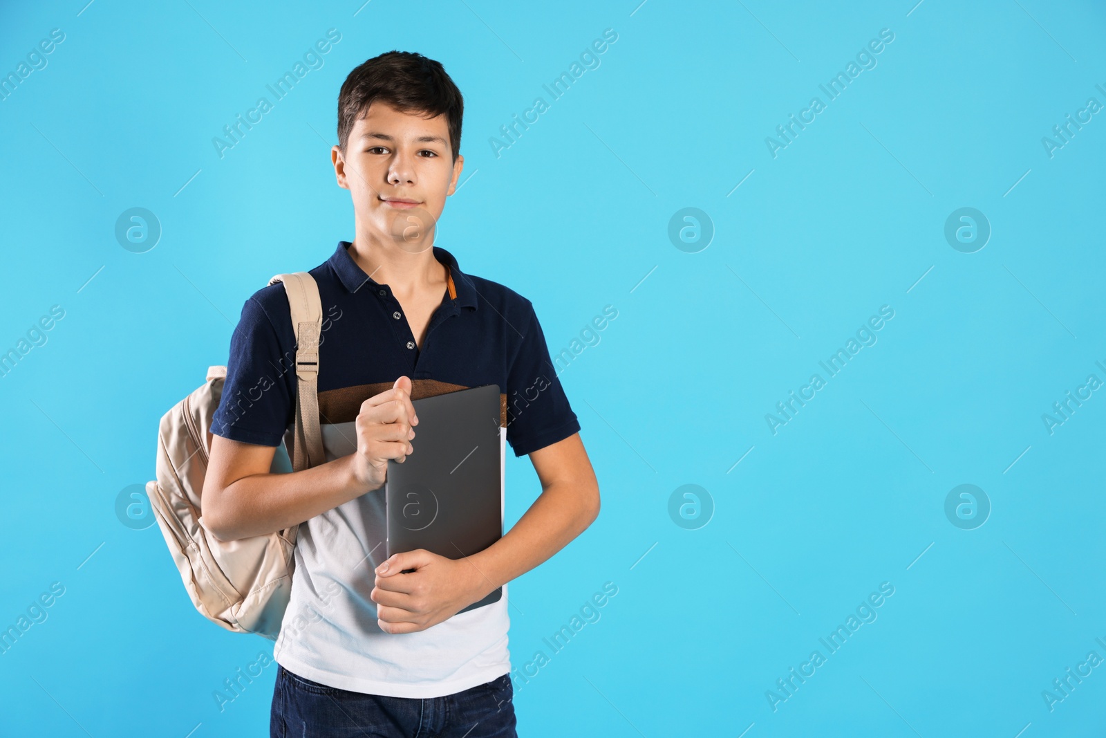 Photo of Portrait of teenage boy with laptop and backpack on light blue background, space for text