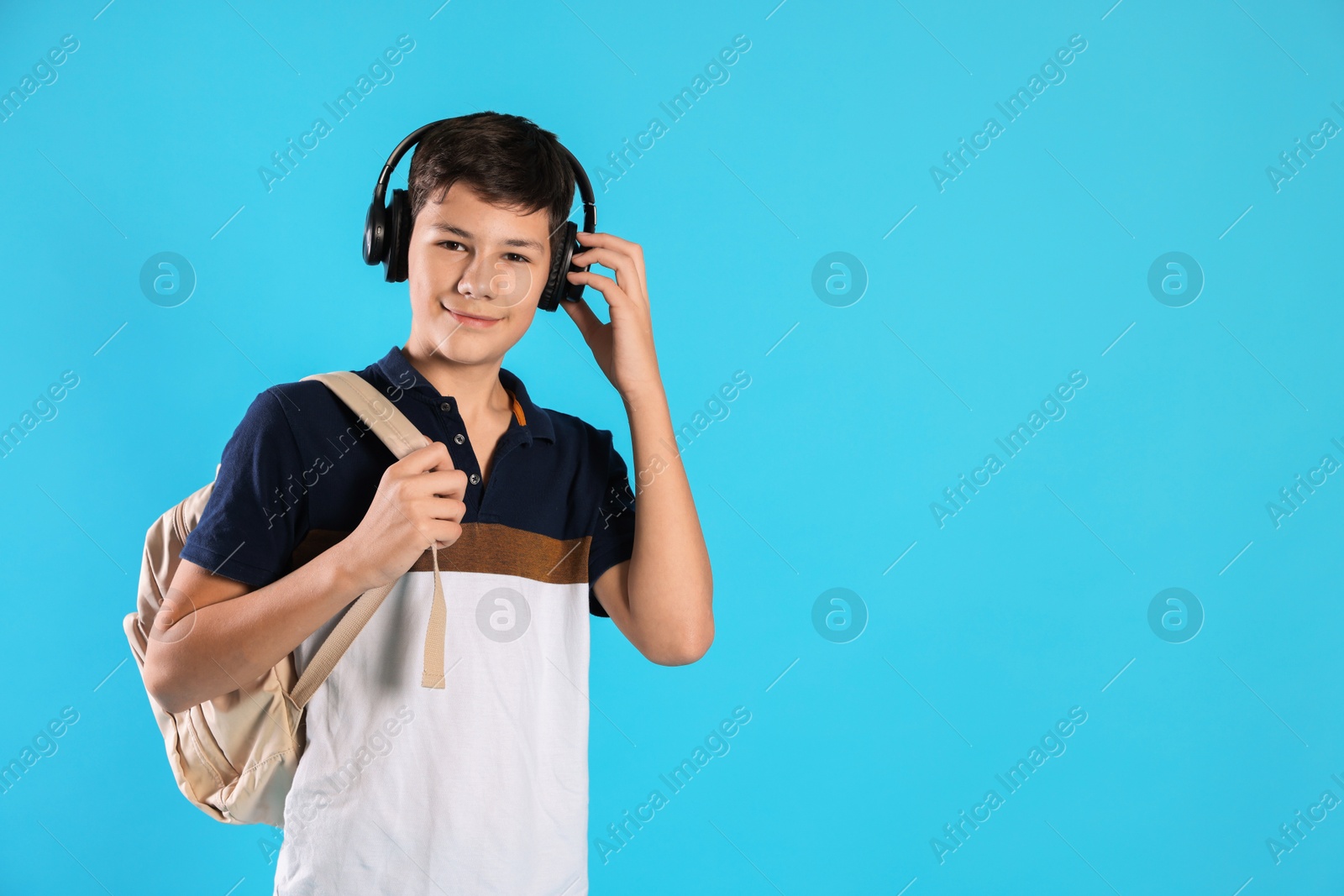 Photo of Portrait of teenage boy with headphones and backpack on light blue background, space for text