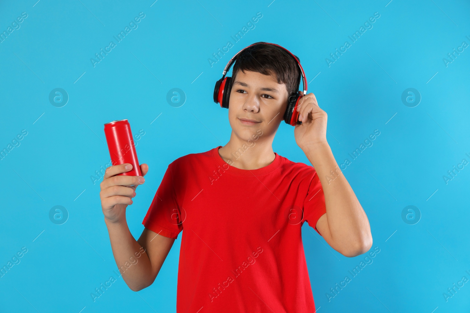 Photo of Portrait of teenage boy with can of drink and headphones on light blue background