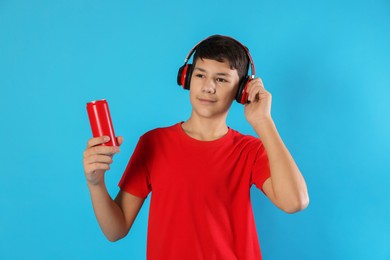 Photo of Portrait of teenage boy with can of drink and headphones on light blue background