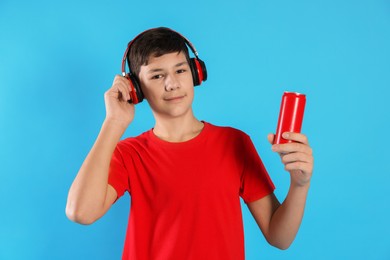 Photo of Portrait of teenage boy with can of drink and headphones on light blue background