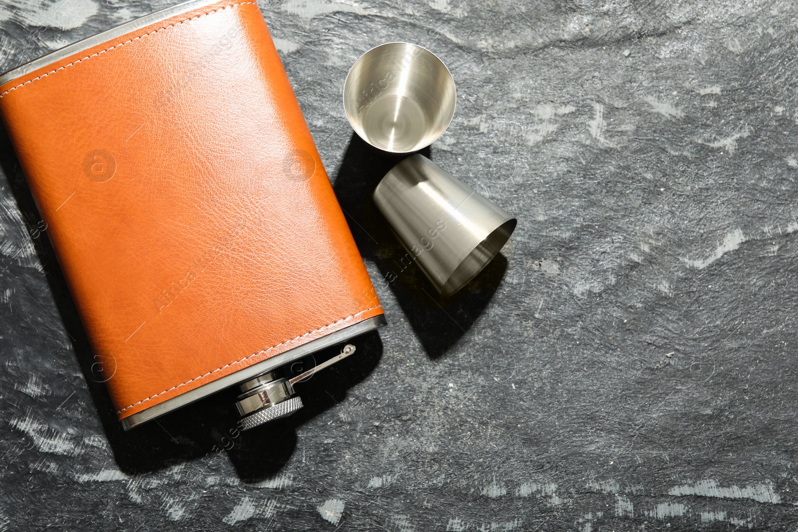 Photo of Hip flask and cups on dark table, flat lay. Space for text