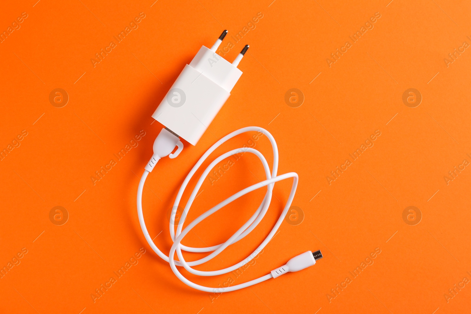 Photo of USB power adapter with charge cable on orange background, top view