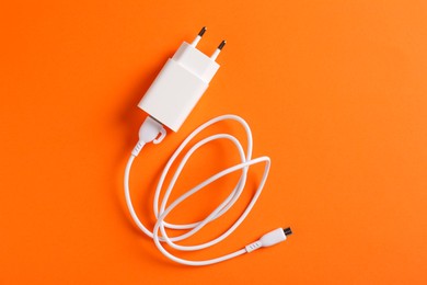 Photo of USB power adapter with charge cable on orange background, top view